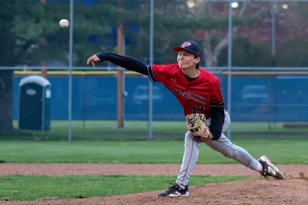 Pitcher releasing the ball toward home plate at dusk