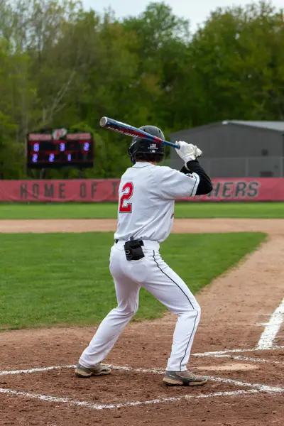 Batter watching a pitch with the scoreboard behind him