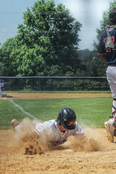 Runner diving into third base in a cloud of dust