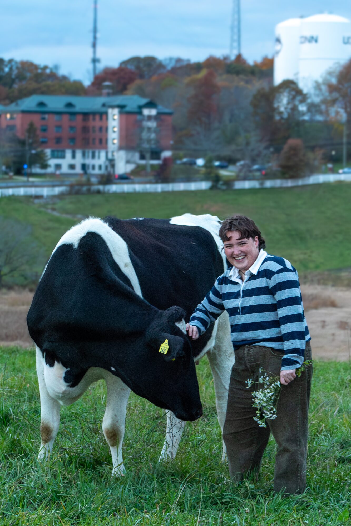 Molly senior portrait, laughing next to a cow with the water tower behind
